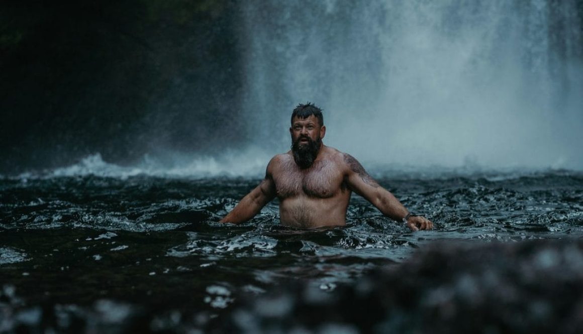 a man standing in the water in front of a waterfall